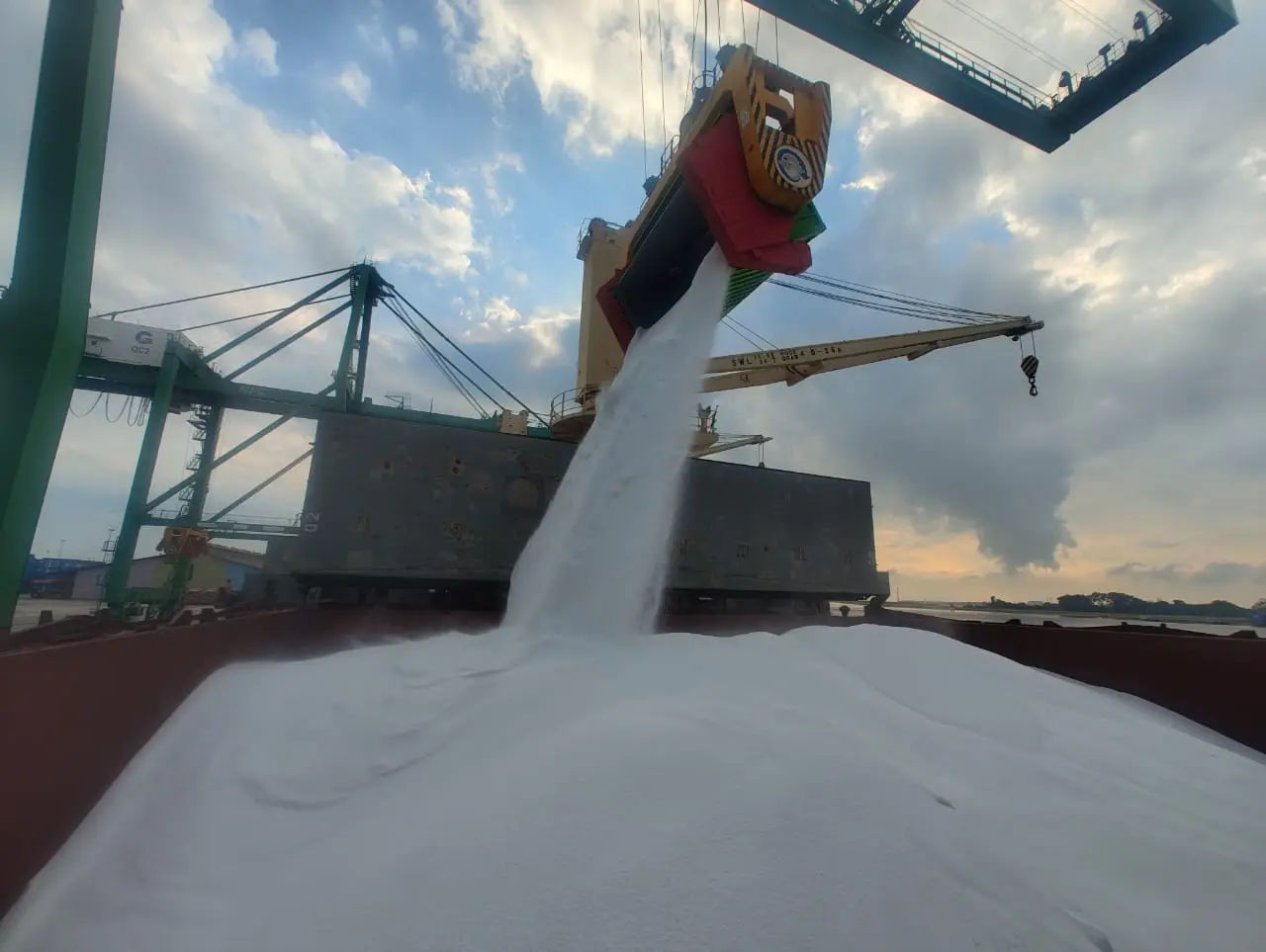 Grab crane pouring fertiliser into a vessel hold at the load port